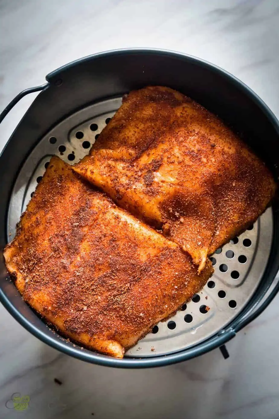 2 pieces of seasoned salmon in the air fryer basket before cooking