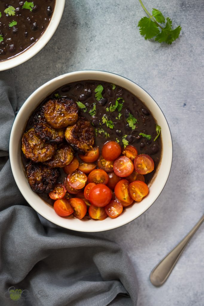 Two servings of cuban black beans made in the instant pot with air fried plantains, tomatoes and sprinkle with fresh cilantro.