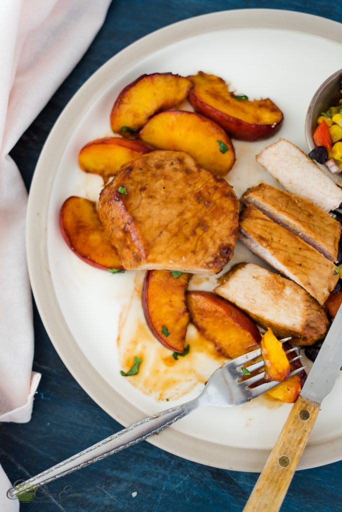 boneless pork chops in air fryer with peaches corn salsa. napkin, fork with a piece of peach and a knife on the side of the plate.