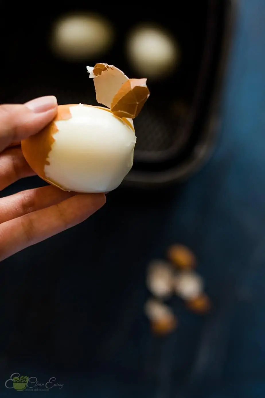 showing how easy it is to peel the shell off of the air fryer hard boiled eggs with the rest of the eggs already peeled in the air basket.