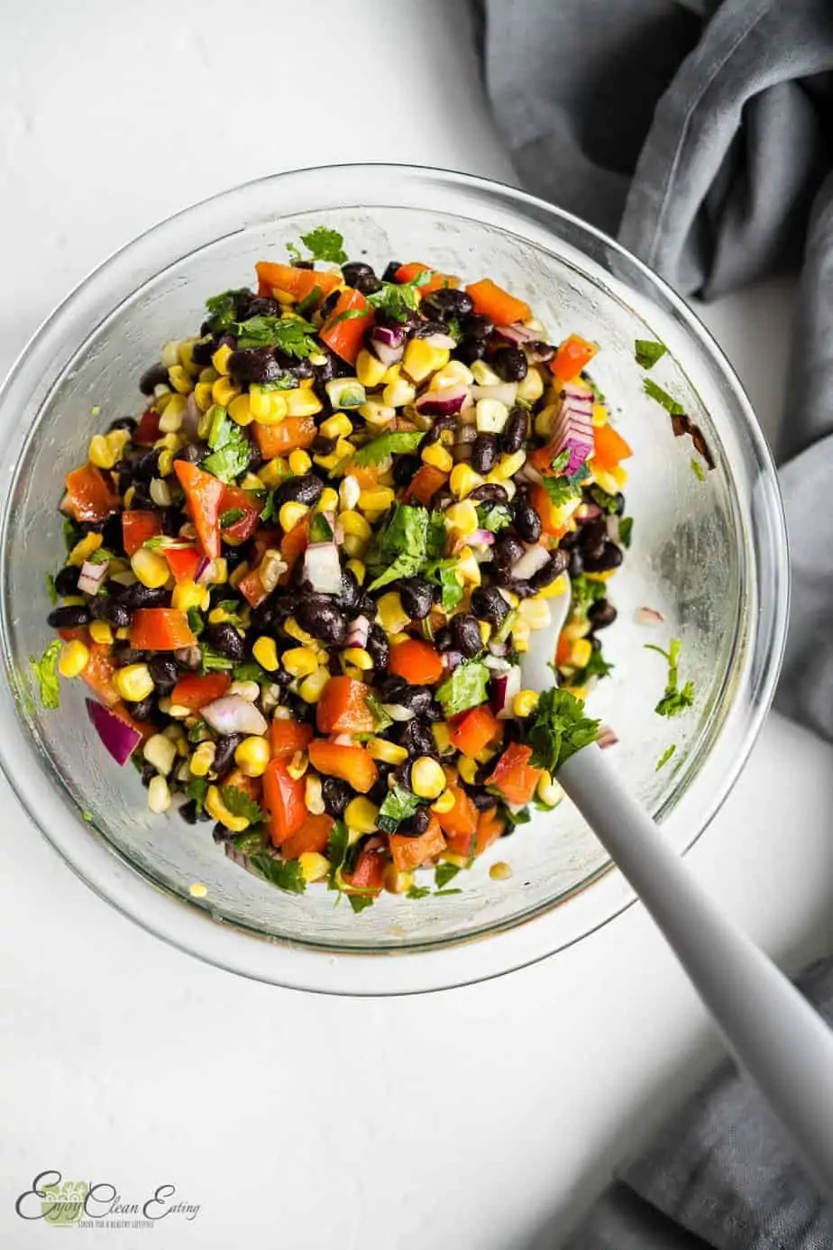 black bean corn salsa in a mixing bowl with a spoon and a dish towel as a prop.