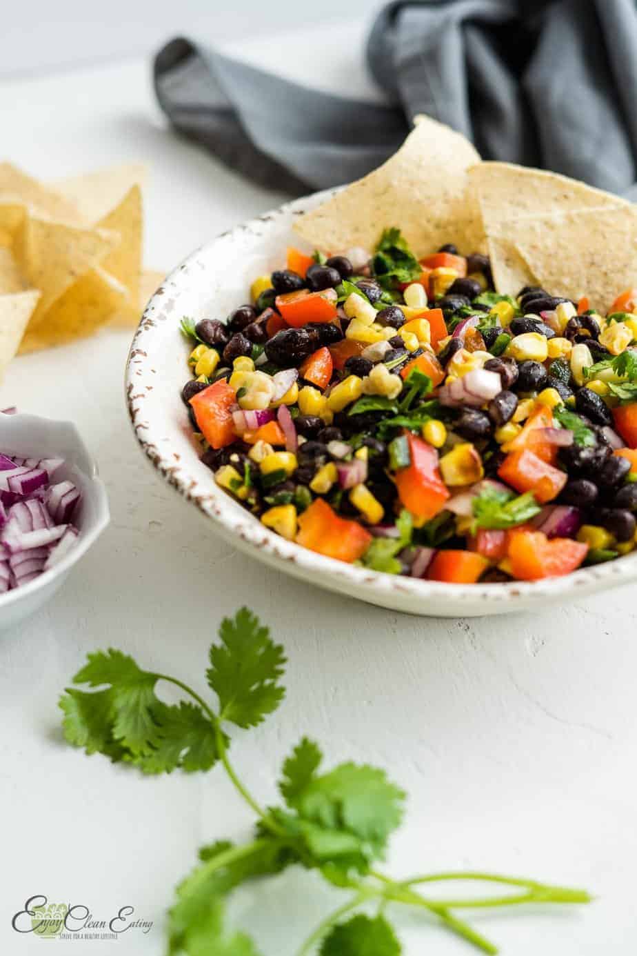 The salsa was serve with tortilla chips on the side there is chopped red onion in a white small bowl, cilantro and some chips on the side.