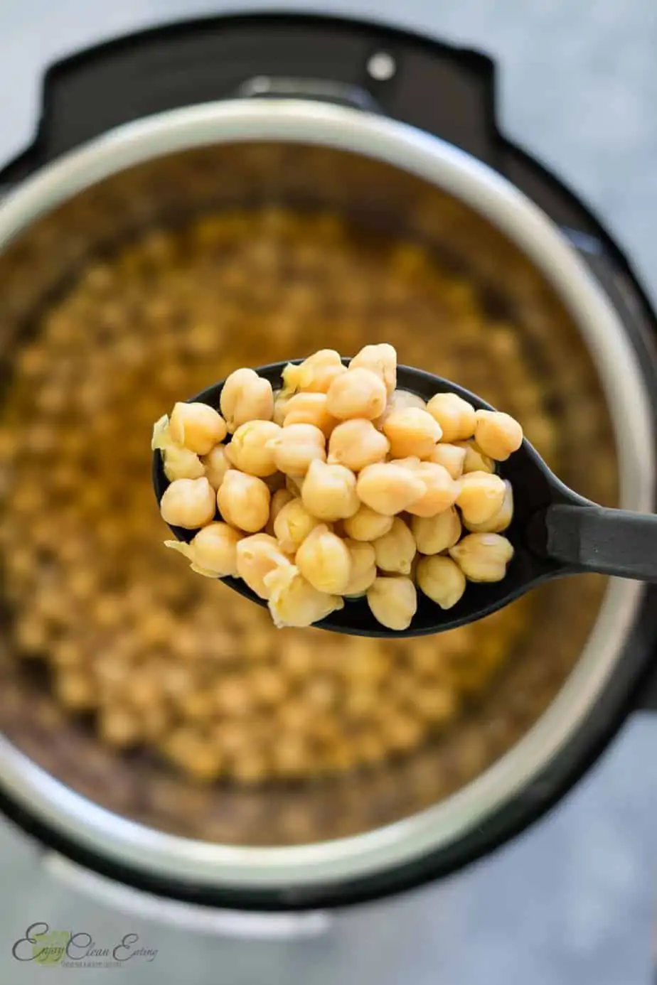 Holding the perfectly cooked chickpeas in the instant pot with a cooking spoon.