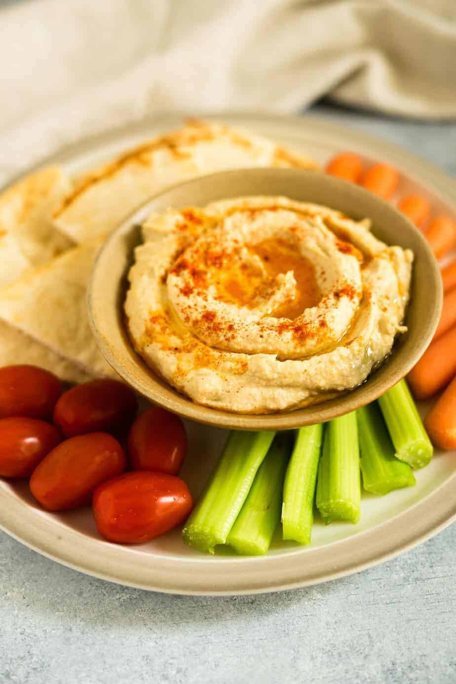 Pressure cooker hummus serve  in a bowl and a plate with veggies and pita bread.