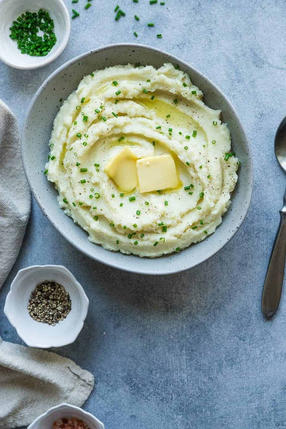 mashed cauliflower instant pot with chives and extra butter. a tiny bowl with chives and another one with black pepper.