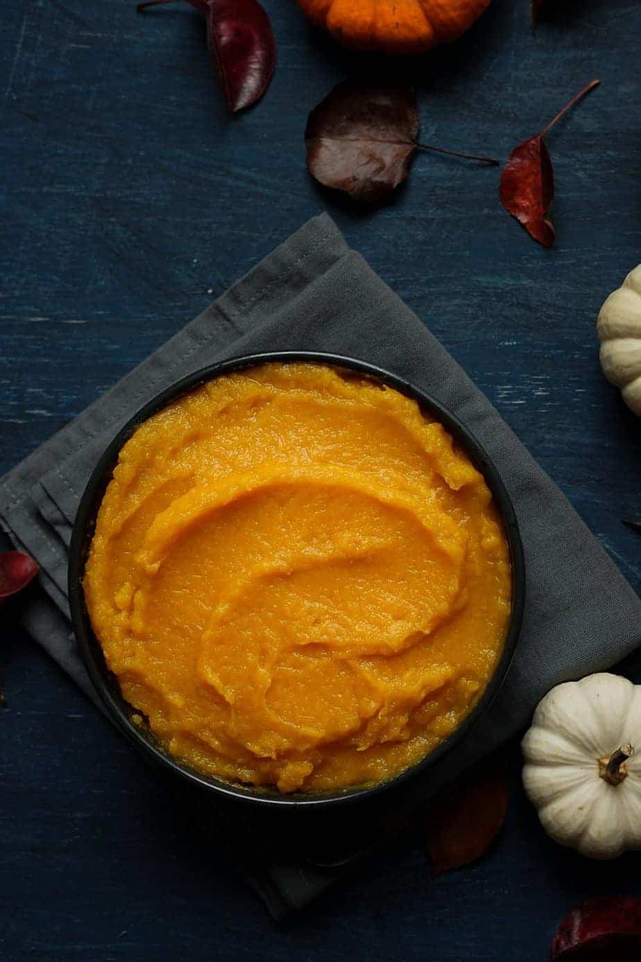 Fresh homemade pumpkin puree made using the instant pot pressure cooker. serve in a bowl to be store in the refrigerator around the bowl, there are pumpkins and leaves