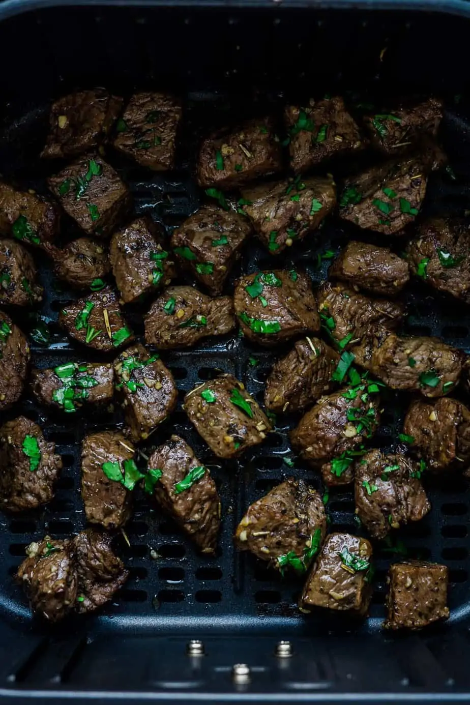 Air fryer steak bites inside the basket and garnish with parsley.