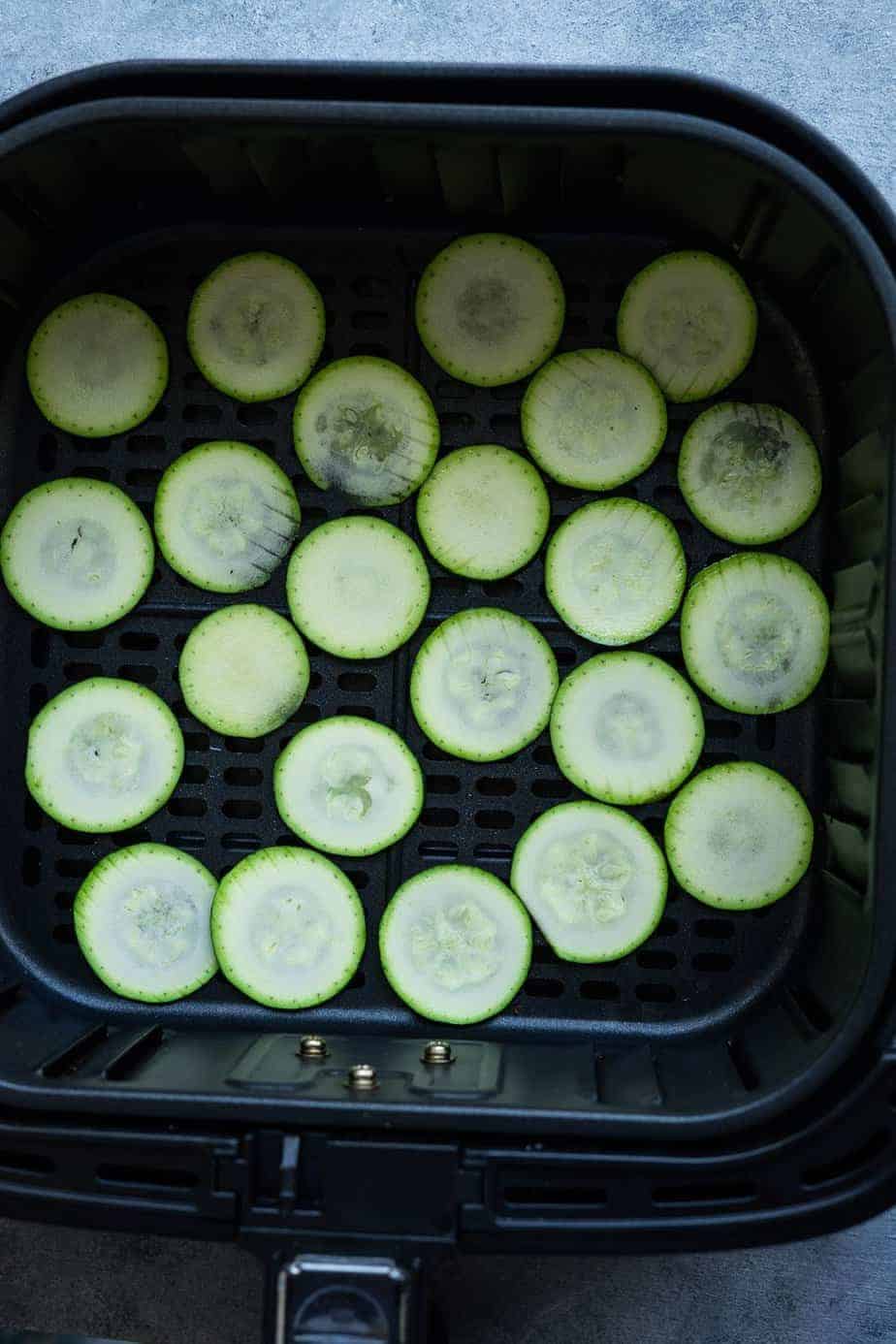 sliced zucchini inside the air fryer basket.