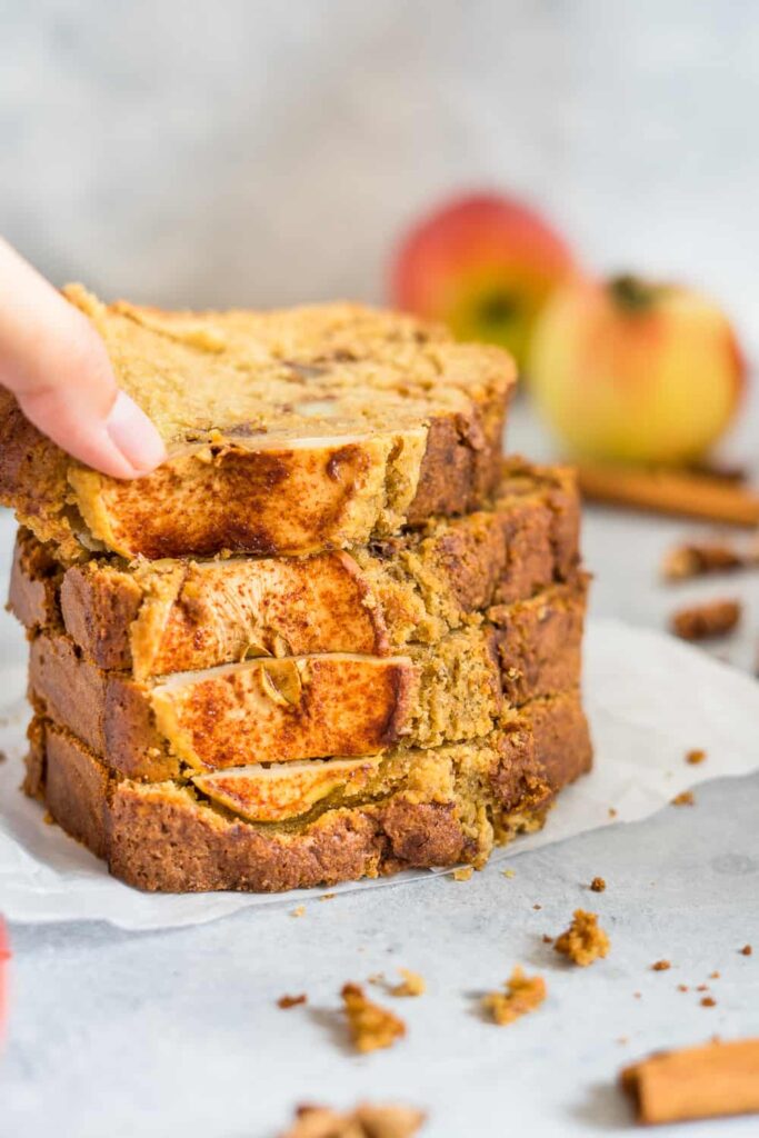 Slices of cinnamon apple bread recipe, some scrambled around and some apples and fall spices on the background.