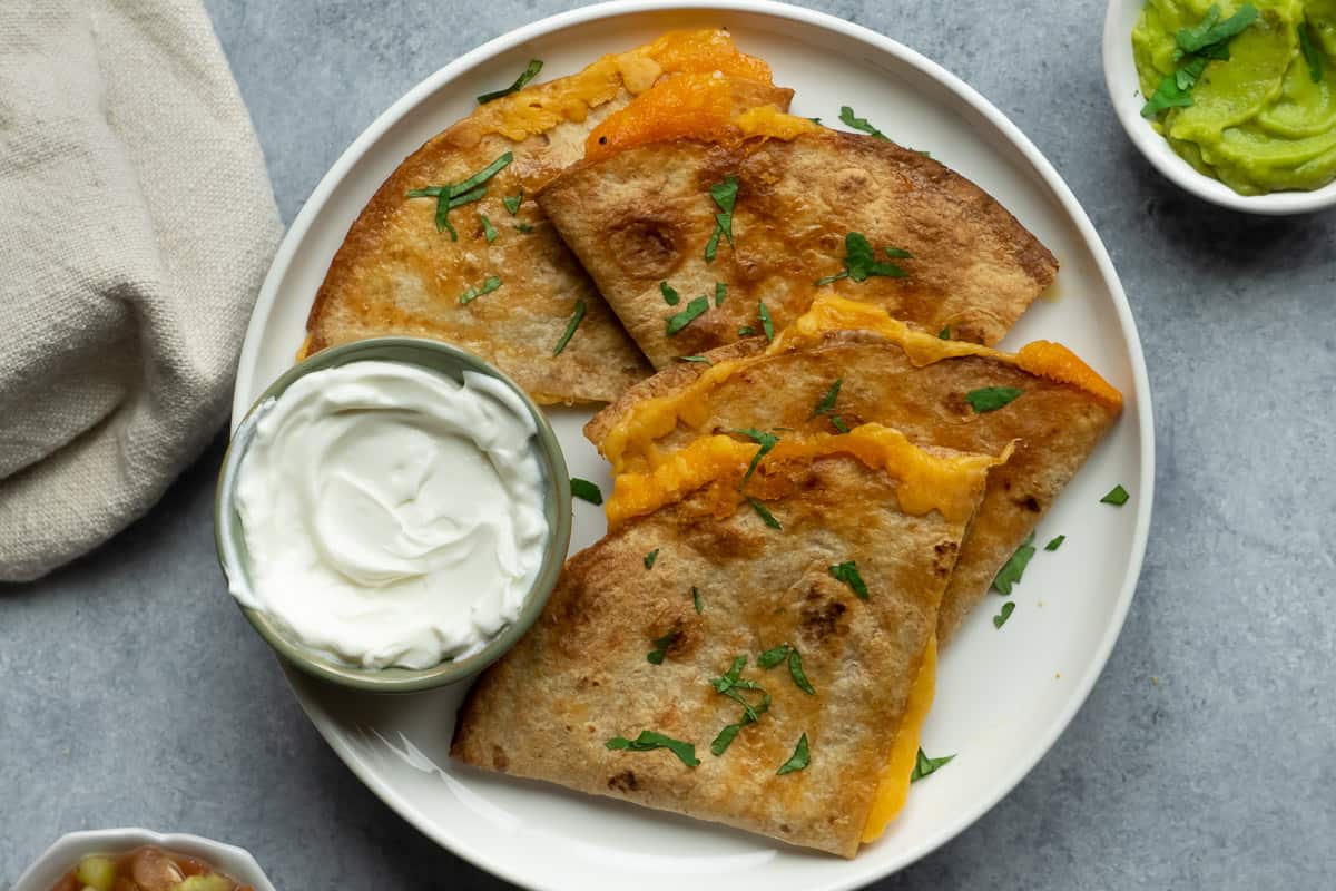 Air fryer cheese quesadilla serve with sour cream, guacamole and salsa.