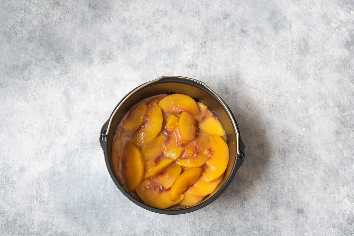 mixing the peach slices in a 7 inches baking dish.