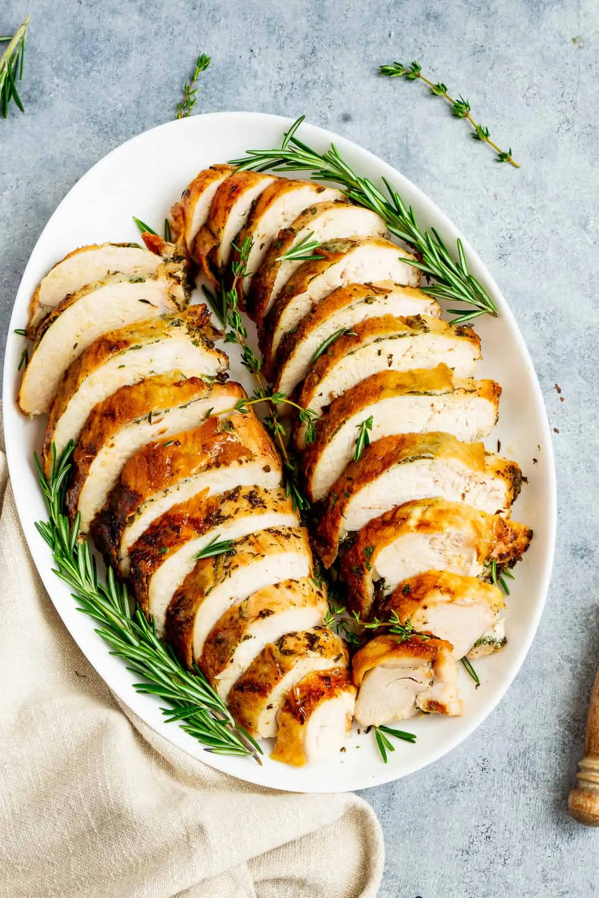 Air fryer roasted turkey breast sliced on a plater with fresh thyme and rosemary.