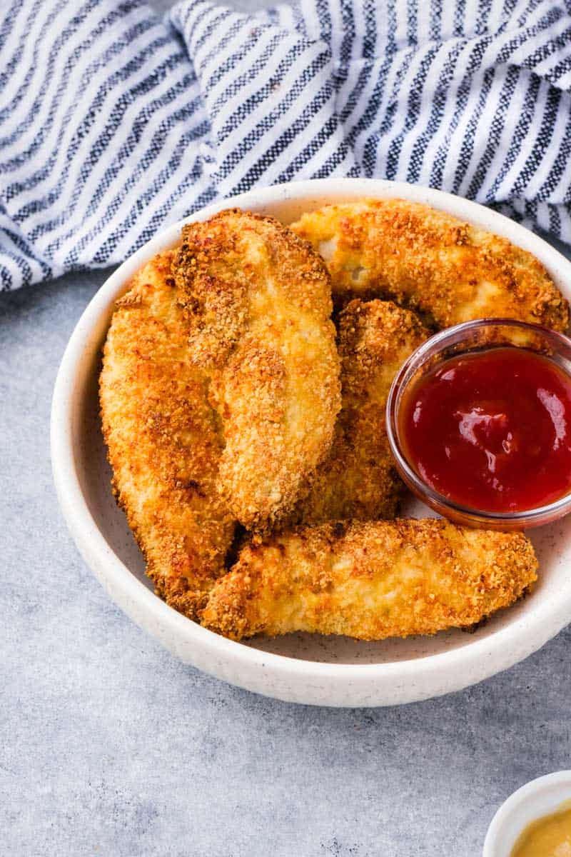 Crispy chicken tenders in a bowl served with ketchup and honey mustard.