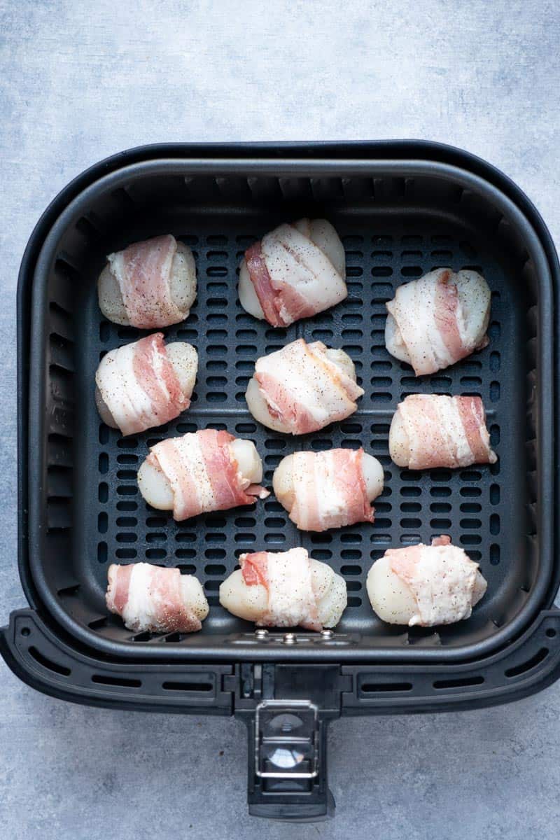 scallops wrapped in bacon inside the air fryer basket before cooking.