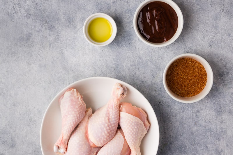 ingredients to make bbq chicken legs. chicken legs, bbq sauce, olive oil and bbq rub.