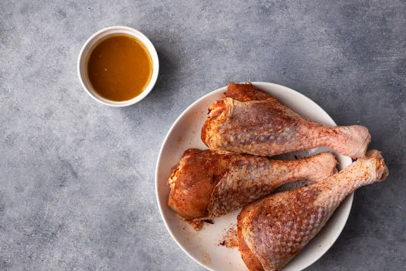 drumsticks seasoned with rub in a bowl and small bowl with the citric maple syrup.
