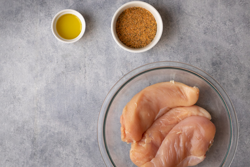 Chicken breasts in a large bowl. Seasoning in a small bowl. Olive oil in a small bowl. i