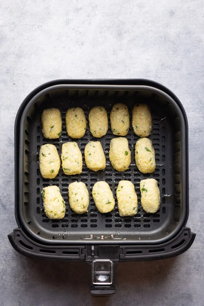 The tots shape inside the air fryer basket before cooking.