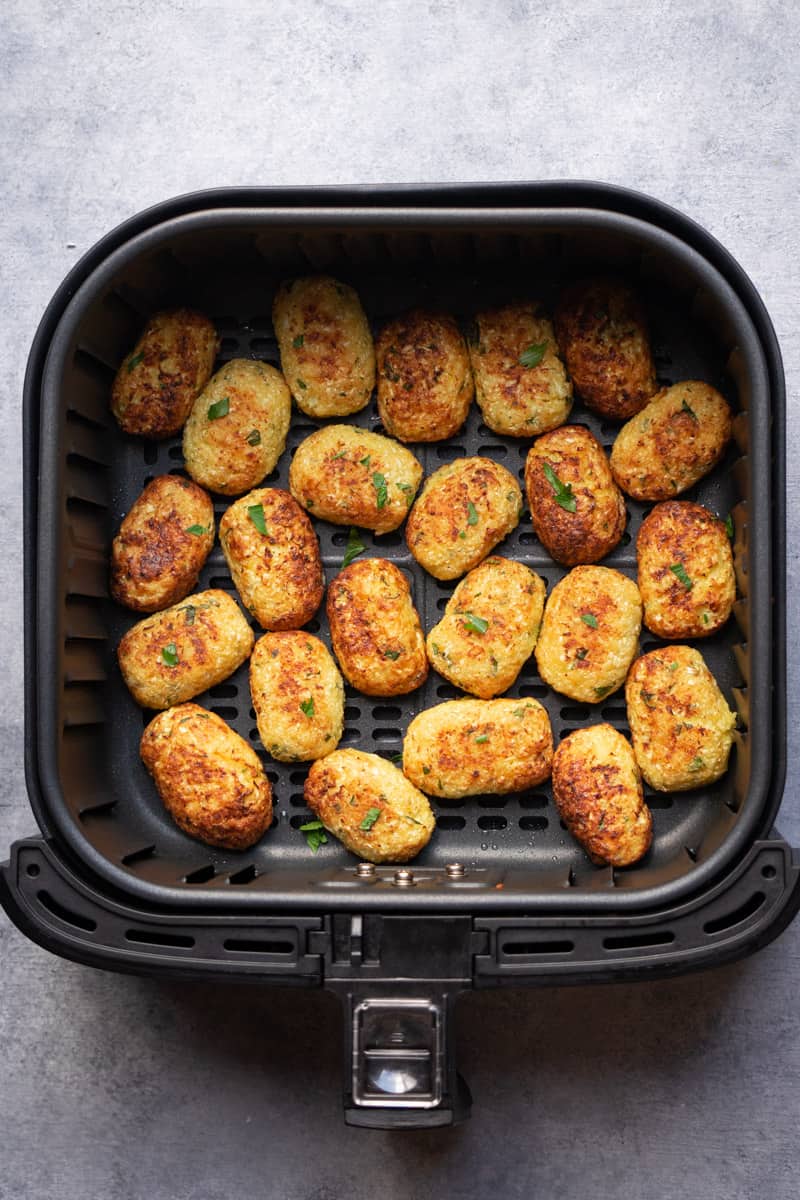 The cauliflower tots in the air fryer basket after cooking.