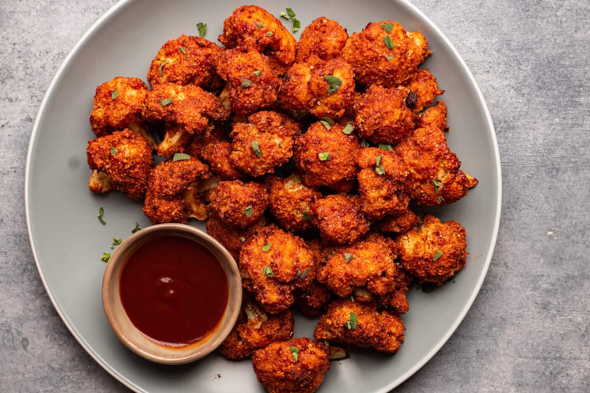 BBQ cauliflower wings served with bbq sauce and sprinkled with fresh herbs.