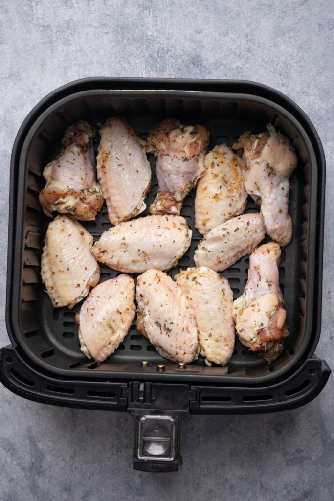 Seasoned chicken wings inside the air fryer basket before cooking.
