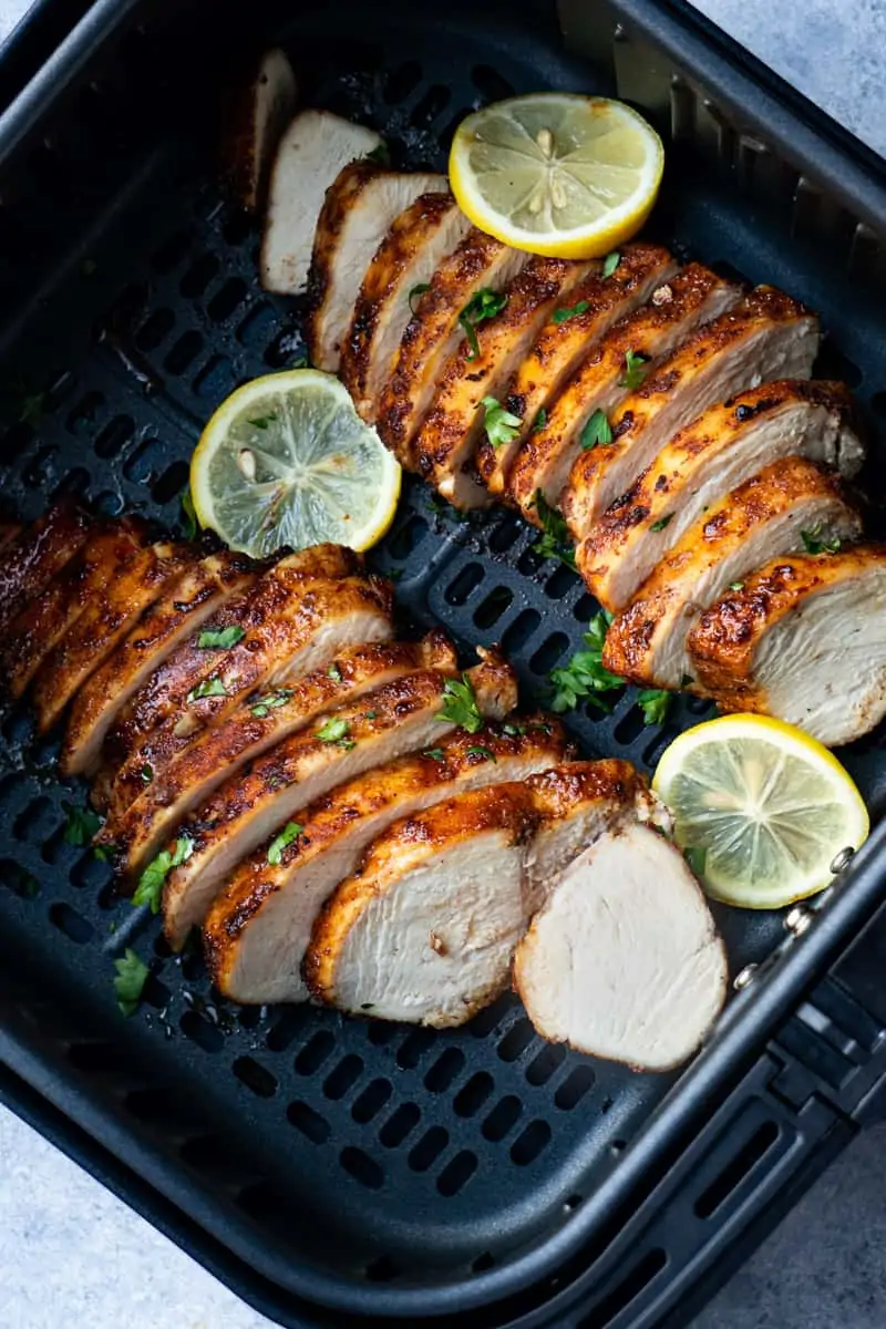Air fryer grilled chicken breast sliced and garnished with lemon and fresh parsley.