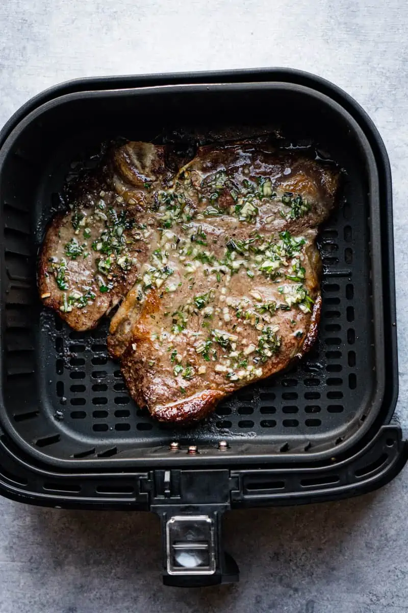 Air fryer porterhouse steak with fresh herbs and butter inside the air fryer basket.