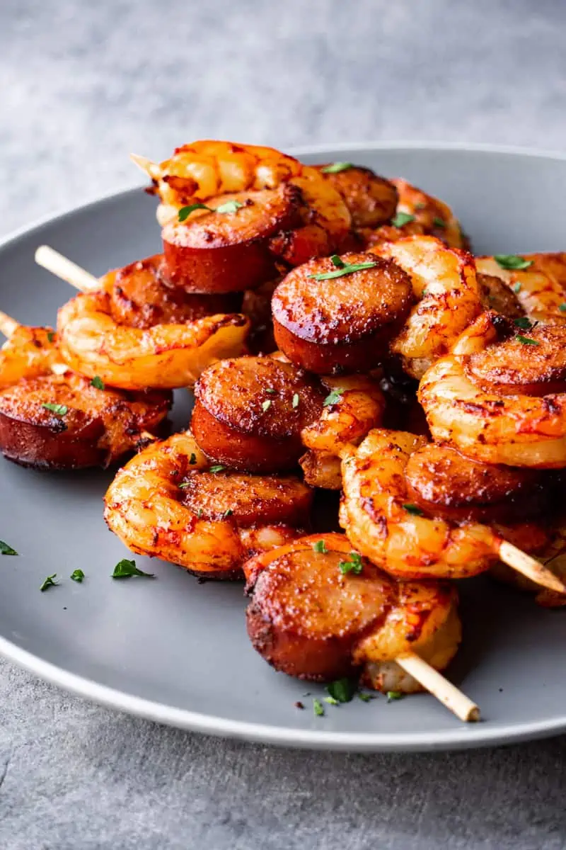 On a plate sprinkled with fresh herbs sausage and shrimp kabobs.