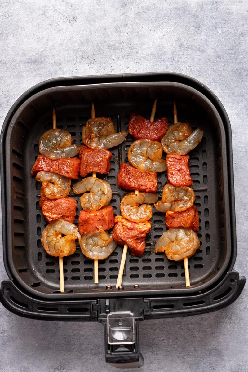 Steak and shrimp kabobs in the air fryer basket before cooking.