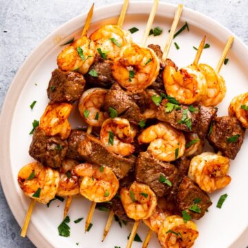 steak and shrimp kabob made in the air fryer, showing them on a plate garnished with fresh herbs