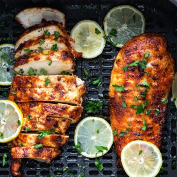 lemon pepper chicken breast in air fryer basket with slices of lemon.