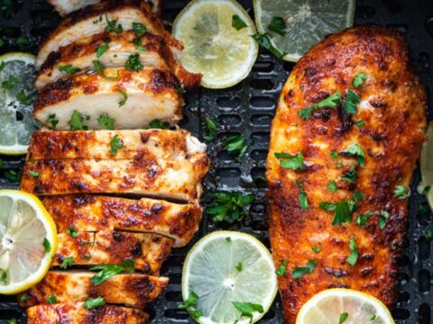 lemon pepper chicken breast in air fryer basket with slices of lemon.