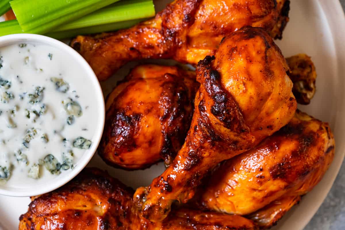 Buffalo chicken drumsticks air fryer serve with blue cheese ranch, celery sticks, and carrots.