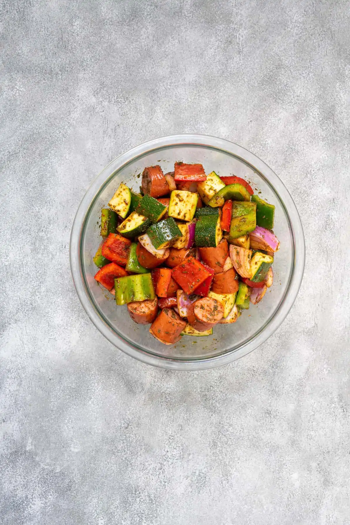 Cut sausage, vegetables, olive oil, and seasoning in a large bowl.