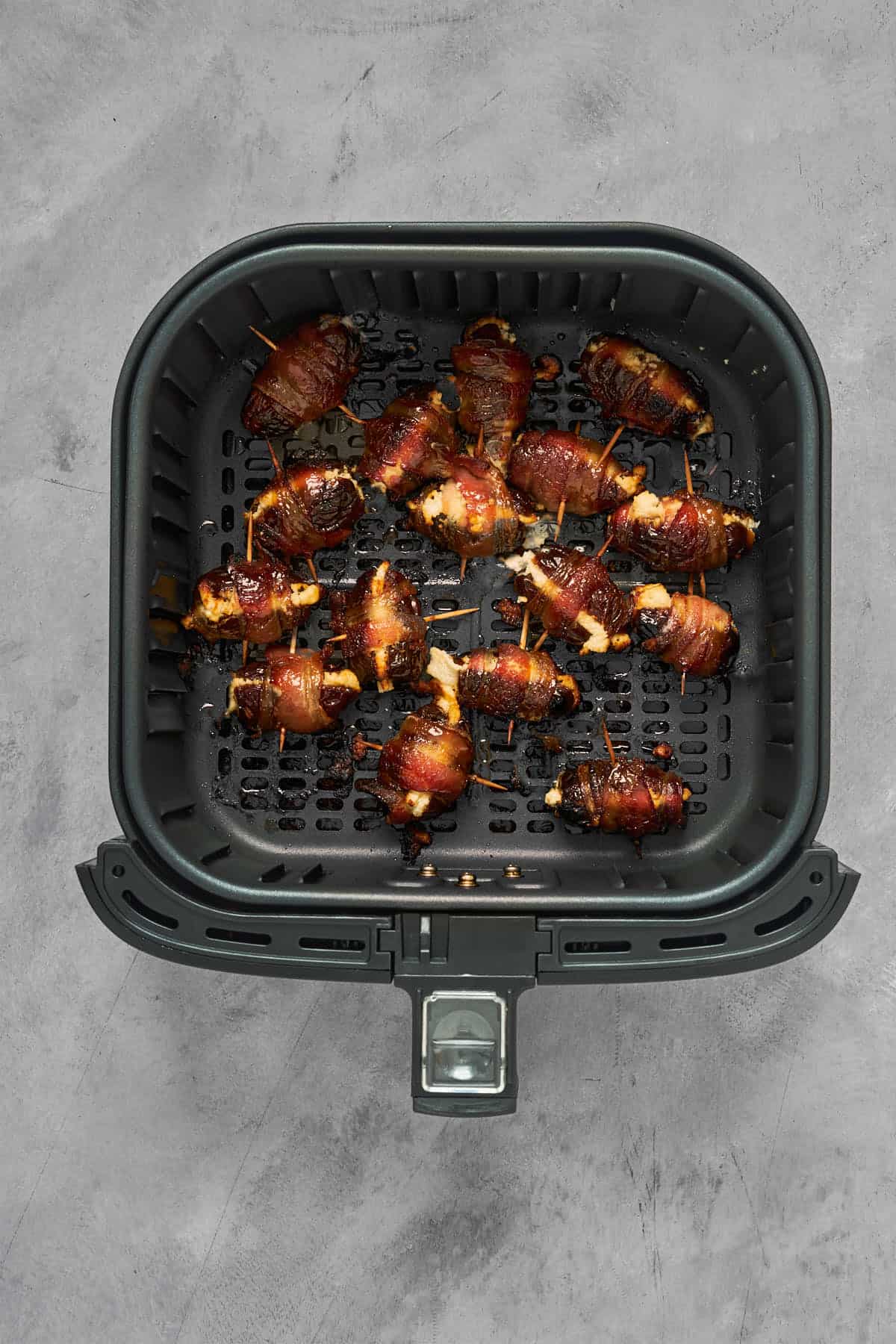 Air fried wrapped dates with crispy bacon inside the air fryer basket after cooking.