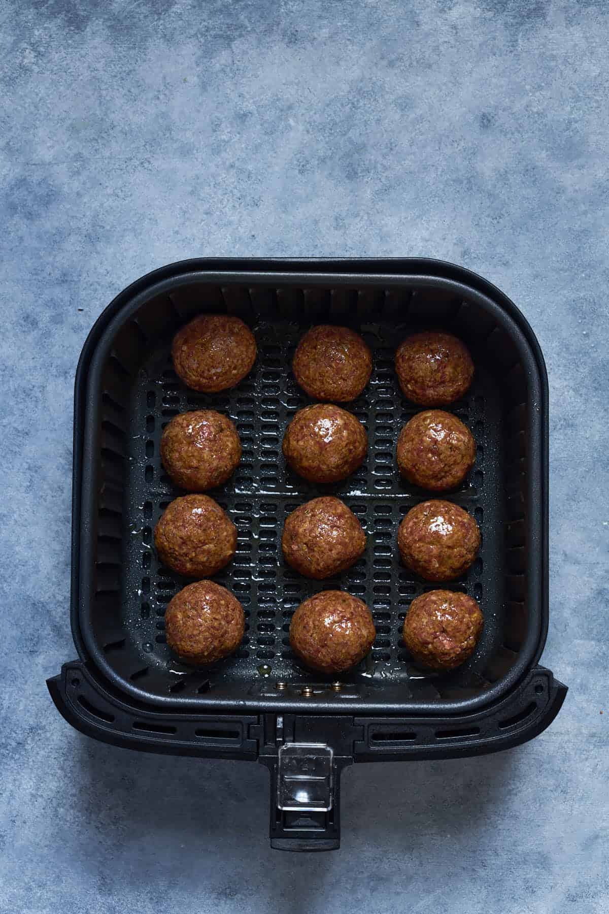 Meatballs inside the air fryer basket before cooking.