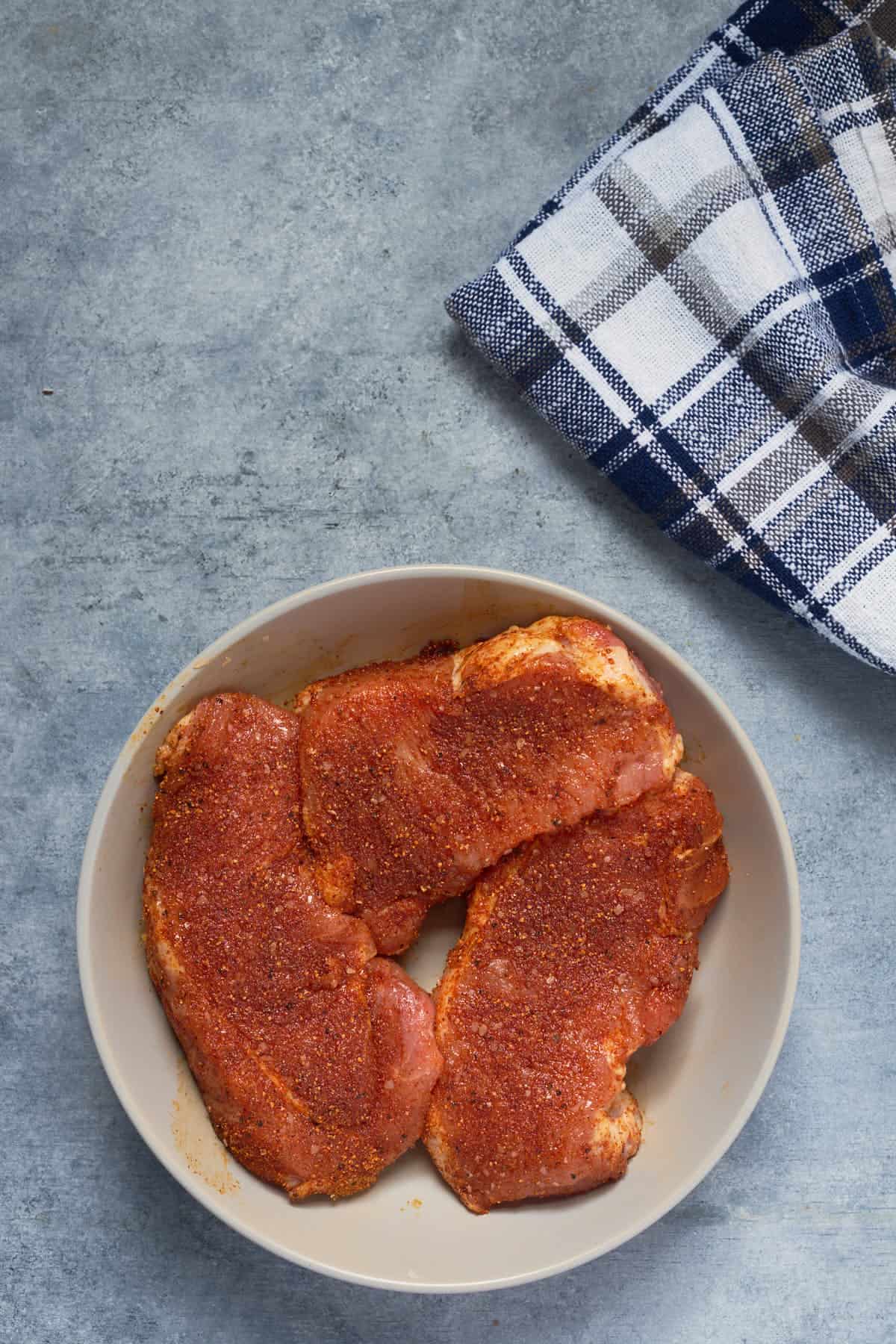 Boneless pork chops sprinkled with oil and rubbed with BBQ seasoning, salt, and pepper.