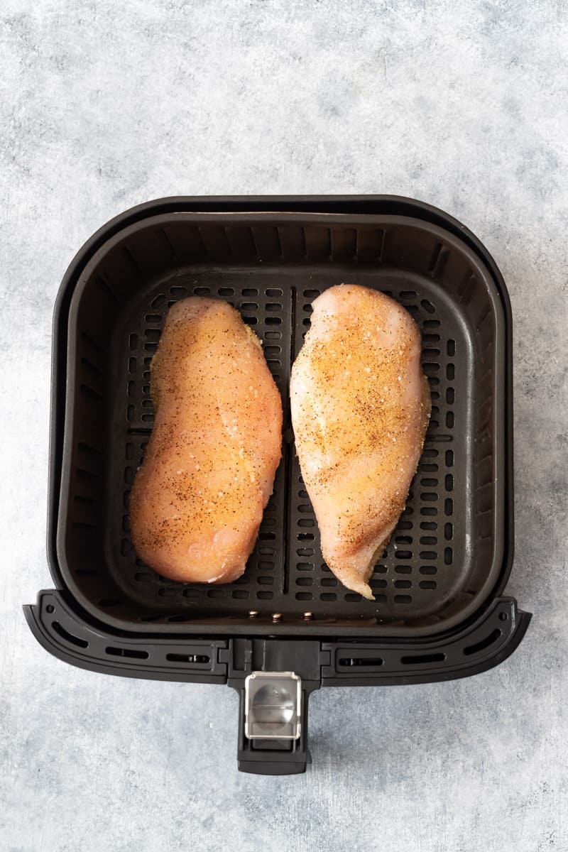 Uncooked chicken breasts with garlic powder, salt, and pepper in the air fryer.