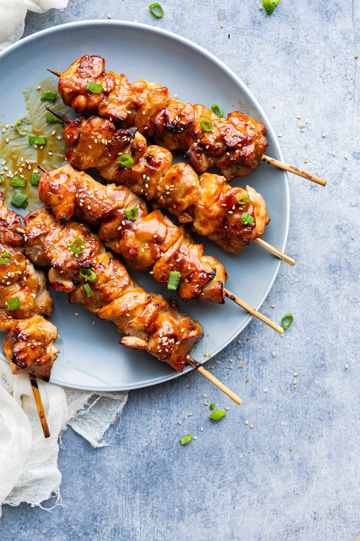Teriyaki chicken skewers sprinkled with sesame seeds and green onion served on a plate and brushed with extra teriyaki sauce.