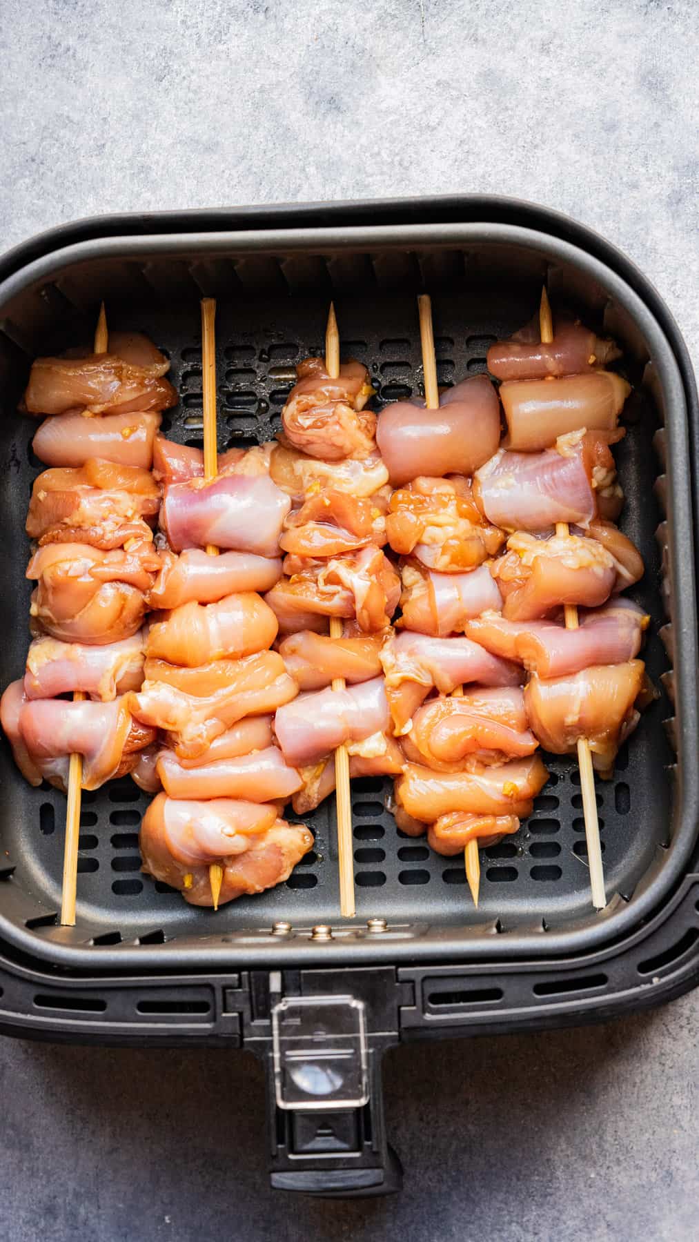 Uncooked marinated chicken skewers in the air fryer basket.