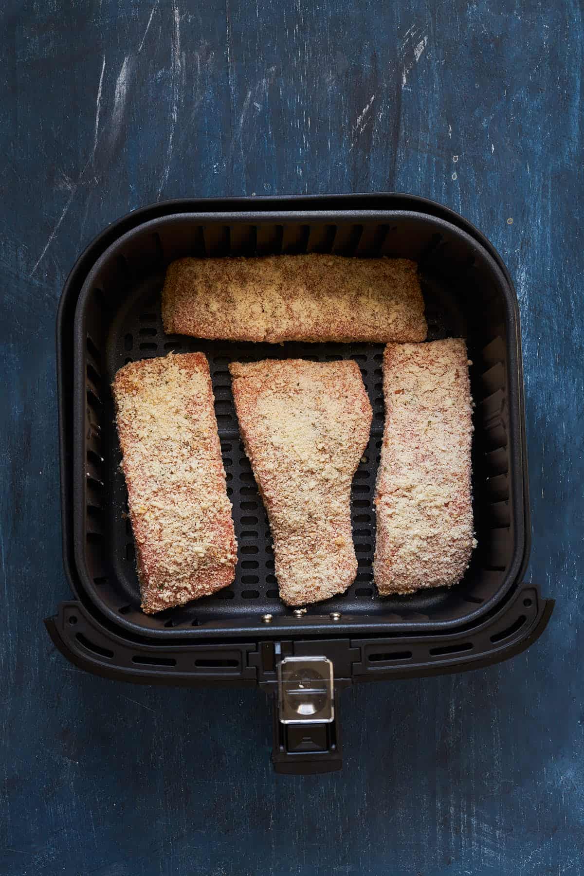 Breaded salmon in the air fryer basket before spraying with oil.