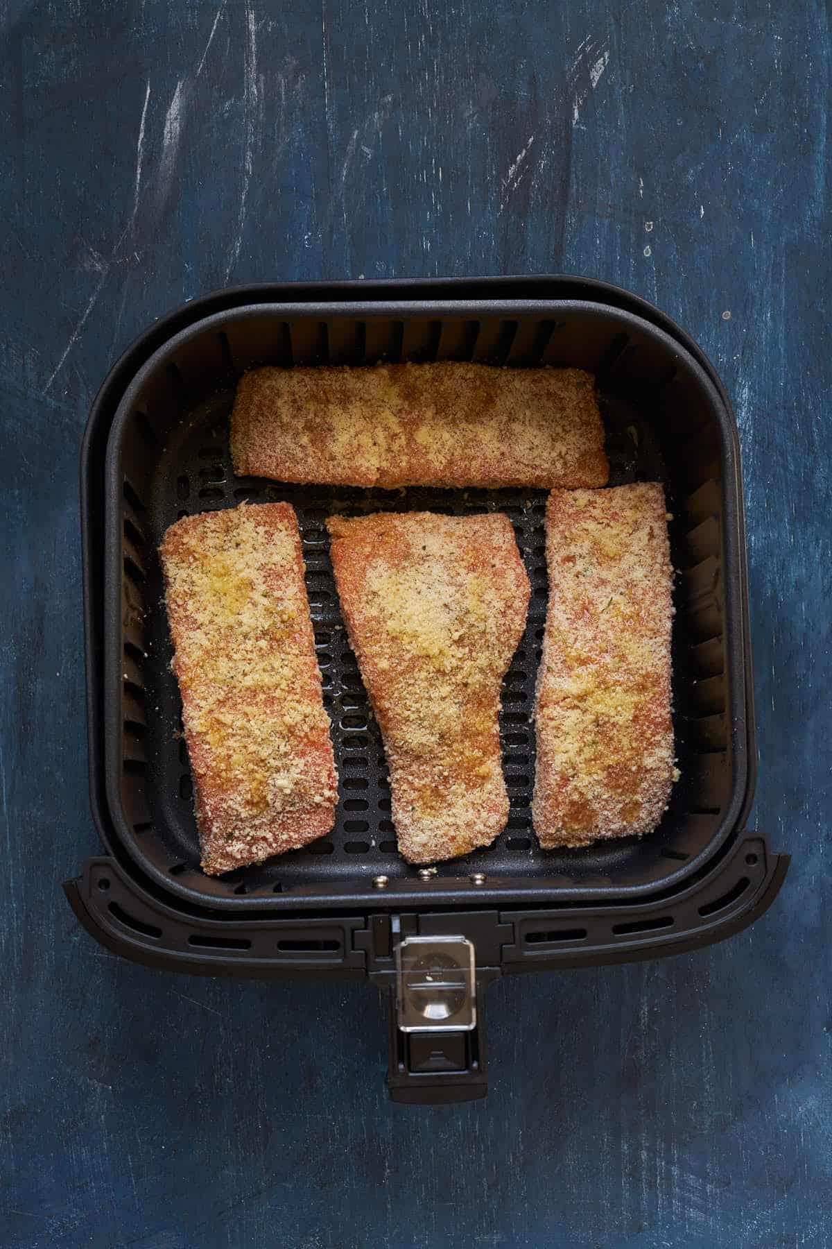 Breaded salmon in the air fryer basket after spraying with oil.