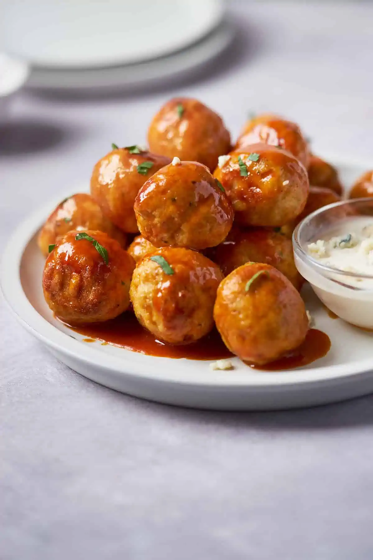 Air-fried buffalo chicken meatballs are served on a plate, sprinkled with fresh herbs, and on the side, blue cheese ranch with crumbled blue cheese on top.