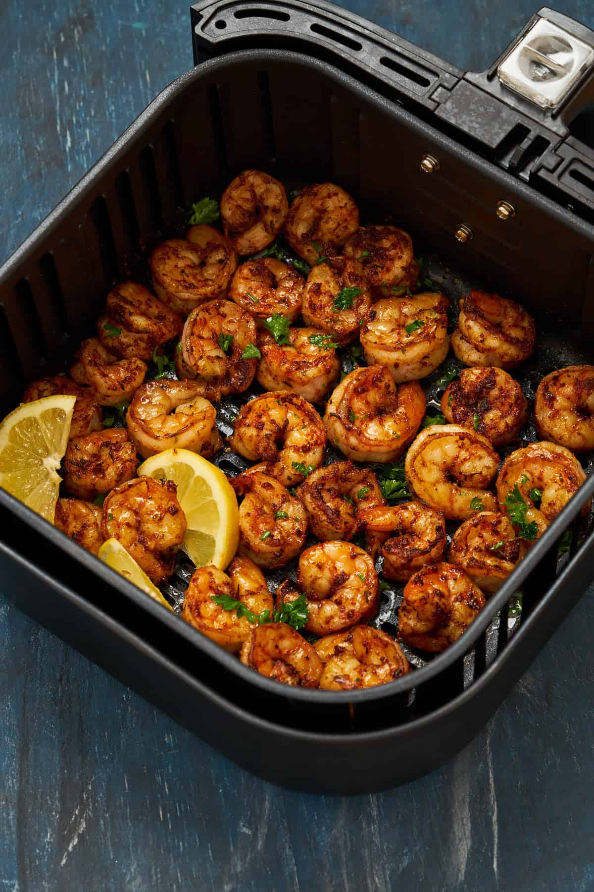 Cooked cajun shrimp with lemon in the air fryer basket.