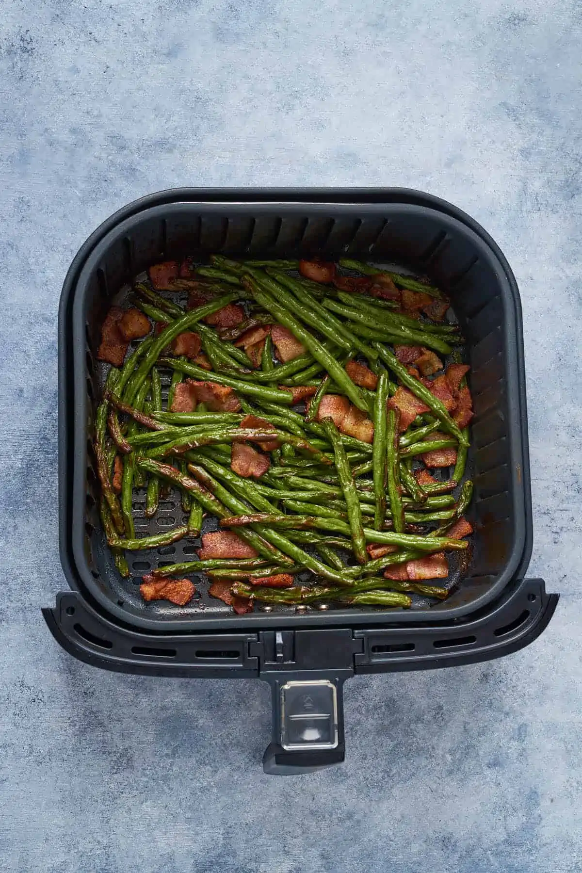 Air fried green beans and bacon in the air fryer basket.