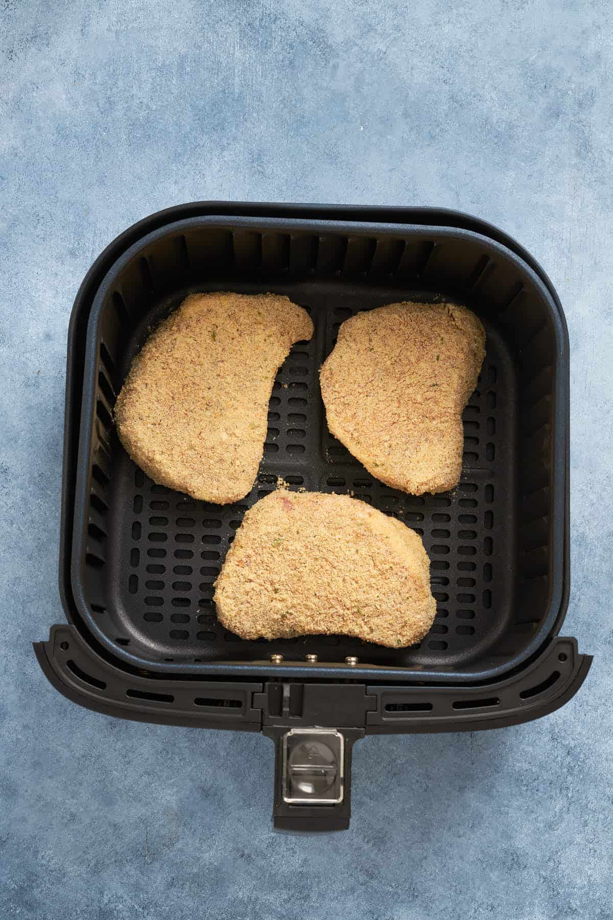 Breaded pork chops before spraying with oil in the air fryer basket.