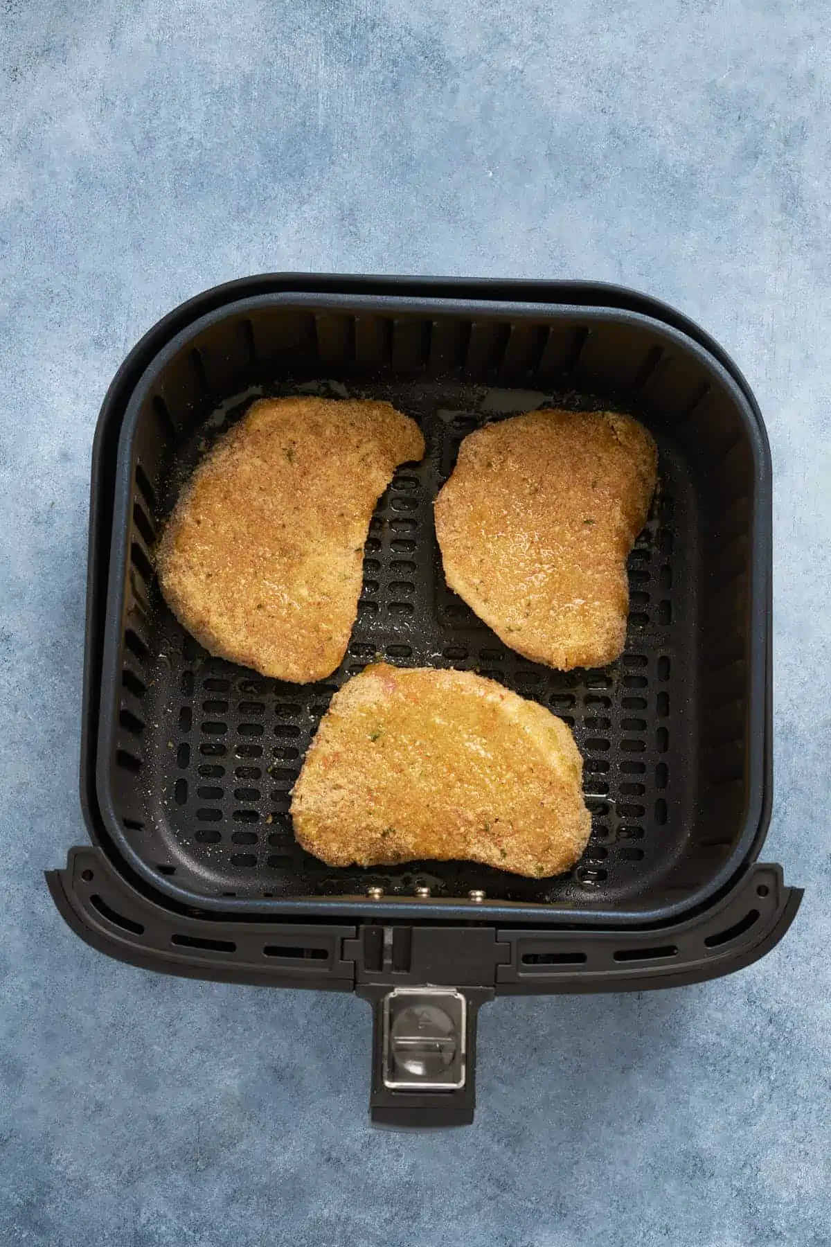 Breaded pork chops after spraying with olive oil in the air fryer basket.