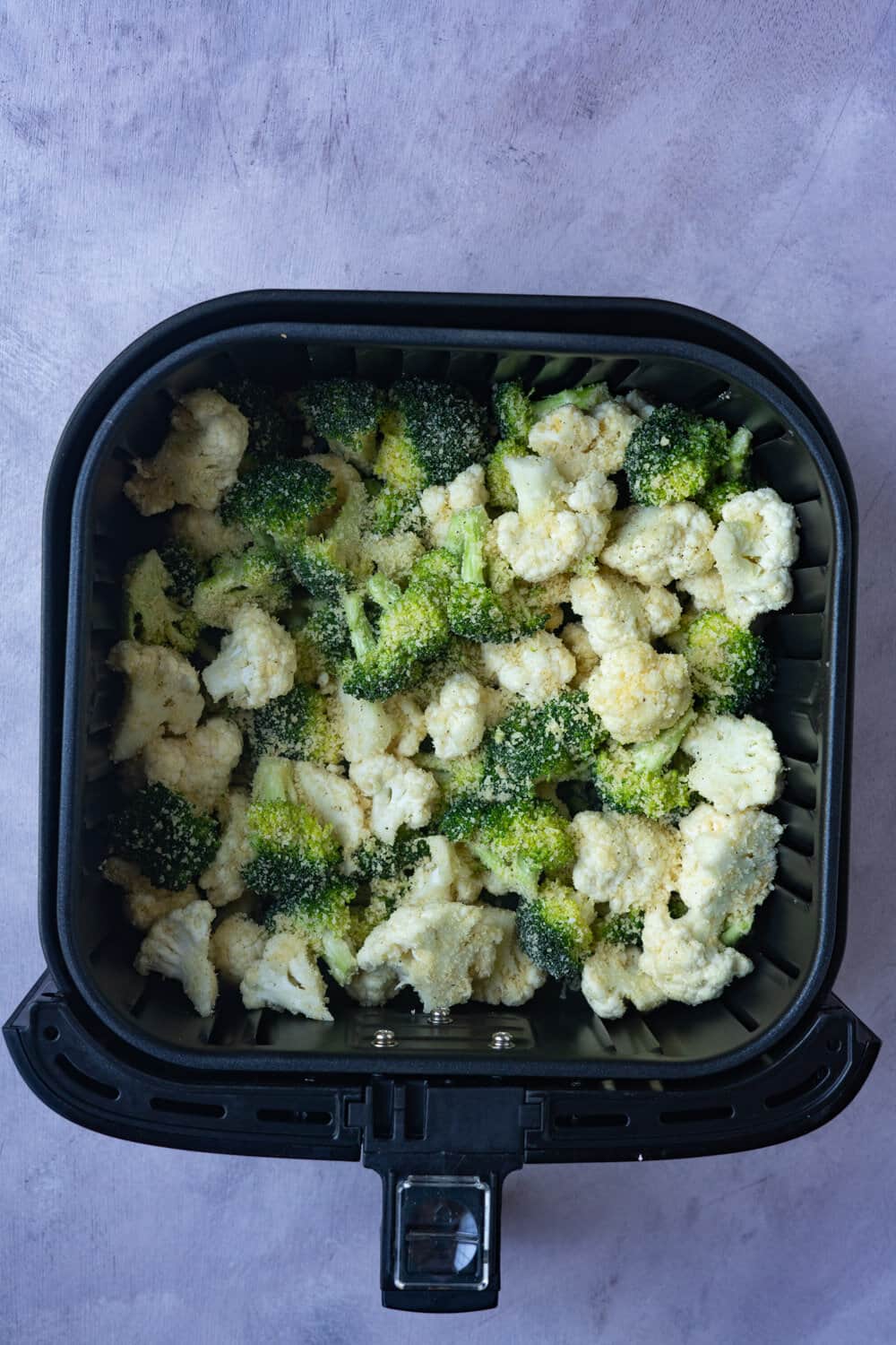 Cauliflower and broccoli in the air fryer basket before cooking.