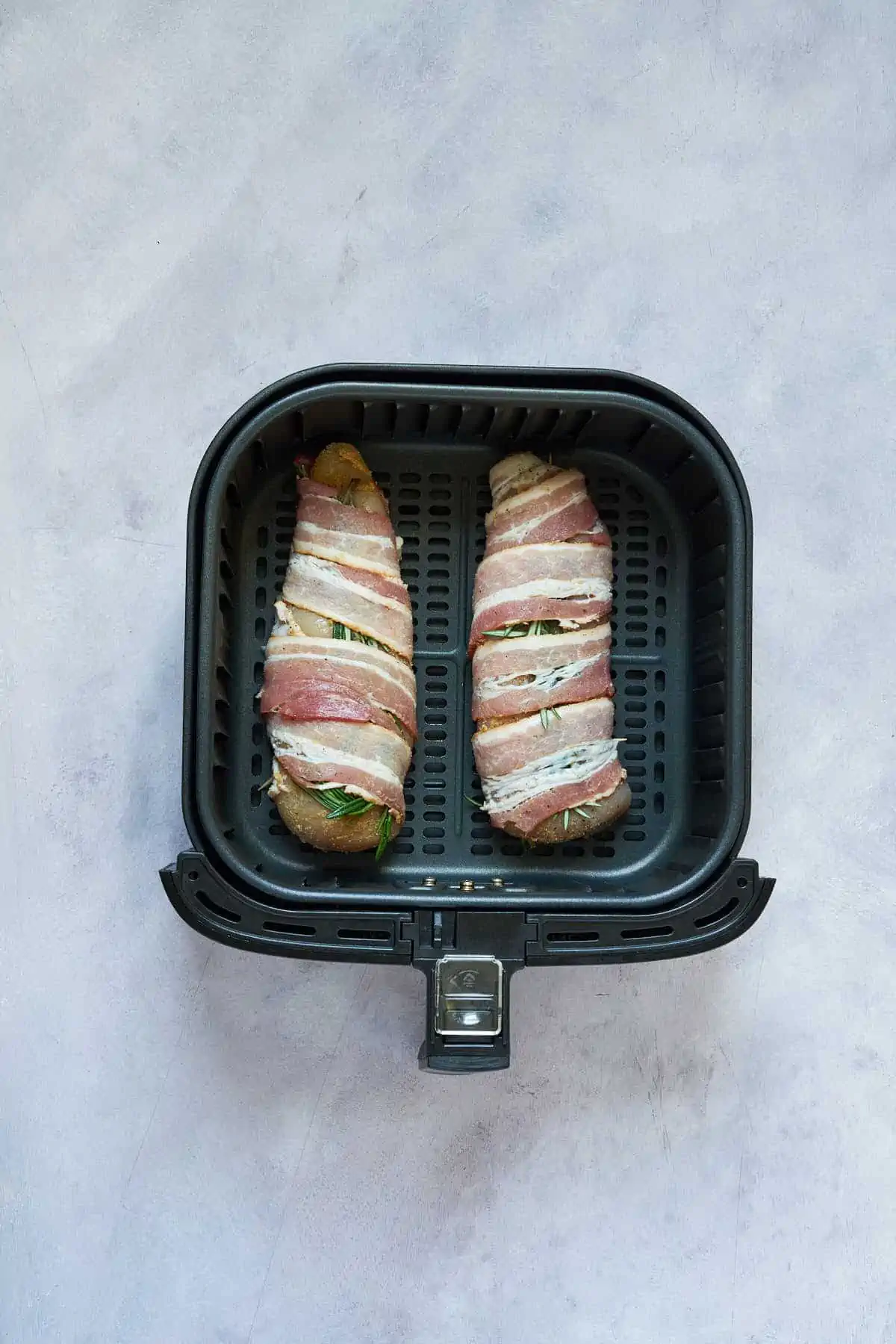 Uncooked bacon wrapped chicken breasts in the air fryer basket.