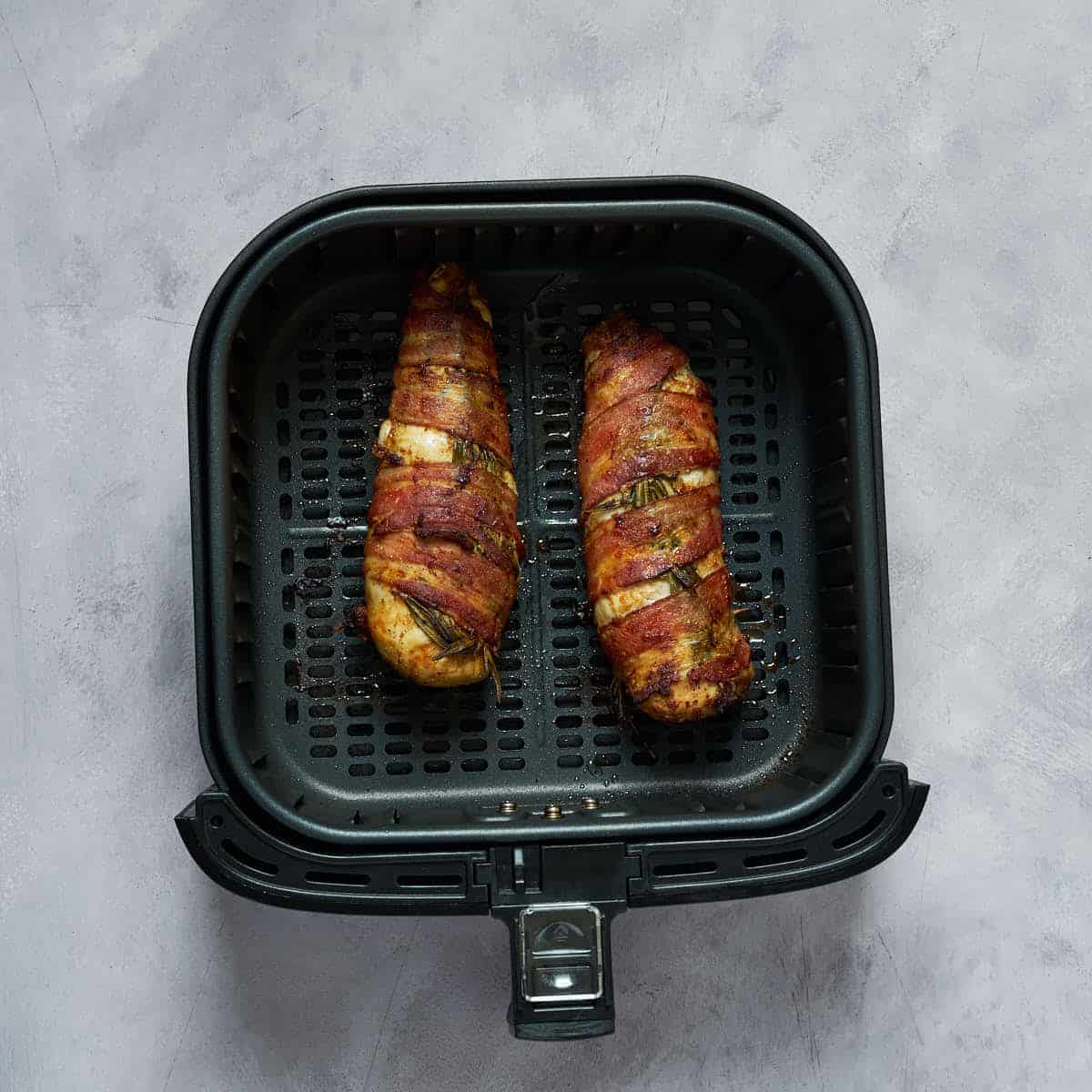 Cooked bacon wrapped chicken breasts in the air fryer basket.